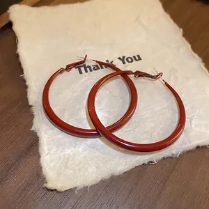 Vintage dark red geometric hoop earrings with glossy finish on textured paper
