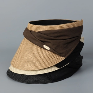 Detail of woven straw sun hats in brown, beige and black with oval metal logo plates