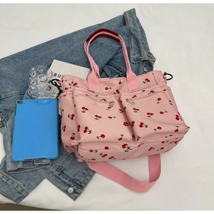 Close-up of pink cherry print canvas tote bag with front pockets on denim background