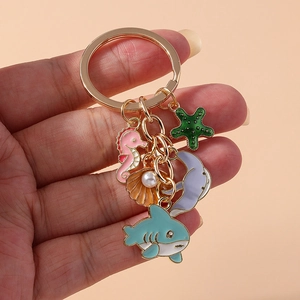Golden keychain featuring ocean enamel charms with starfish and whale hanging on hand