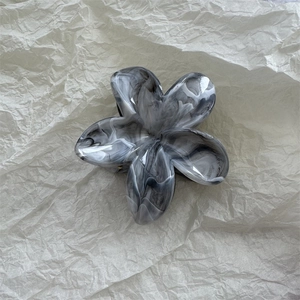 Detail view of flower hair claw clip with black and white marble ink texture on paper