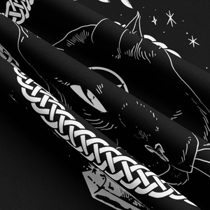 Macro shot of black fabric showing white cat silhouette, celtic knot, and stars