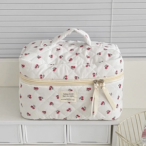 Detail of white quilted cosmetic bag with cherry patterns and ribbon zipper pulls