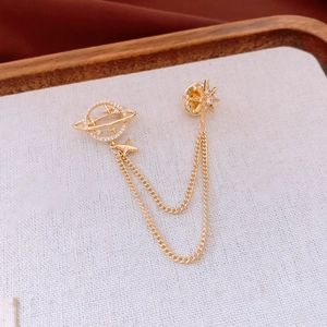 Detail of 14K gold plated Saturn brooch with stars and zircon chains on fabric background