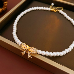 Détail du collier de perles avec pendentif nœud doré serti de strass brillants