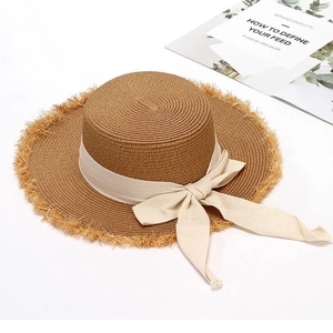 Straw sun hat with flat top, frayed edges and beige ribbon bow for beach vacation