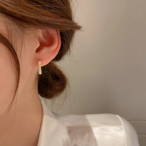 Elegant gold metal bar earrings with small white pearls worn by a model in soft light