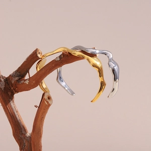 Artistic display of wave-shaped gold and silver stainless steel bangles on wooden branches