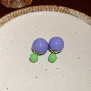 Close-up of purple and green double ball stud earrings on a beige ceramic tray