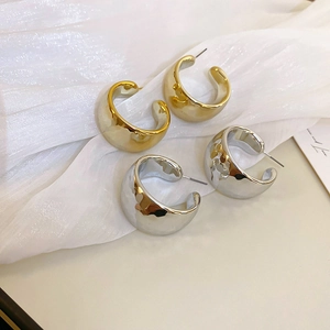 Close-up of polished gold and silver wide C-hoop earrings with elegant diamond patterns