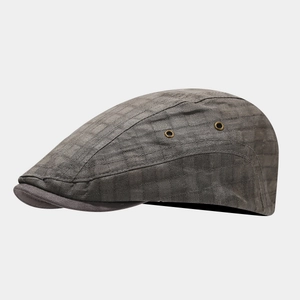 Detail of dark grey retro flat cap showing textured fabric and brass ventilation eyelets