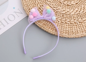 Detail of girls purple headband with mesh bow and colorful pom poms on flat lay