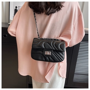 Detail of classic black quilted chain bag worn crossbody by model in professional setting