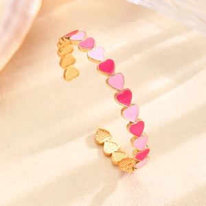 Detalle de un brazalete dorado en forma de C con motivos de corazones en esmalte rosa