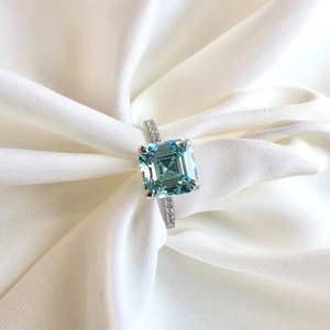 Macro shot of square light blue zircon ring on white silk with micro-pave accents