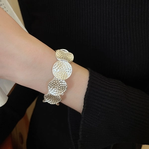 Close-up of silver elastic bracelet with textured circular metal pieces on wrist