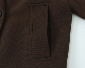 Macro detail of dark brown wool coat showing twill texture and vertical welt pocket