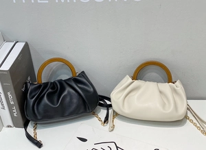 Detail view of cloud-shaped pleated handbags in black and beige with wooden handles