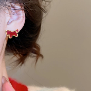 Close-up of a golden dog-shaped stud earring with red enamel inlay on model's ear