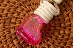 Macro shot of heart-shaped glass bottle with pink liquid and wooden cap on rattan mat