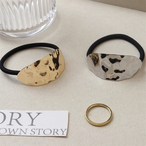 Detail of black hair ties with hammered gold and silver irregular metal charms