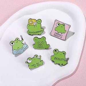 Funny green frog enamel pins set with humorous English quotes on a white ceramic tray