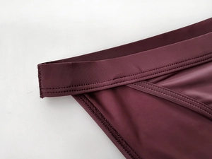 Close-up of double-stitched seams and glossy elastic fabric on dark purple underwear