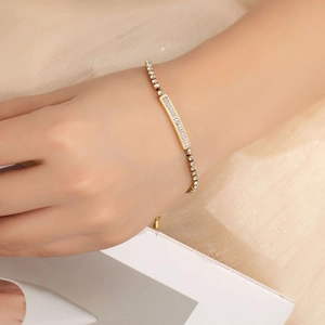 Detail of a gold bracelet featuring a rectangular plate set with sparkling zircons on the wrist