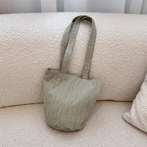 Detail van een groene geplooide stoffen shopper op een crème getextureerde bouclé bank
