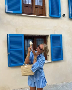 Close-up of blue and white striped shirt set with a beige straw bag in vacation style
