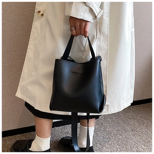 Close-up of black leather bucket bag held by a model against a minimalist background