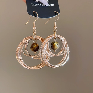 Macro detail of textured golden rings with a polished tiger eye stone bead dangle