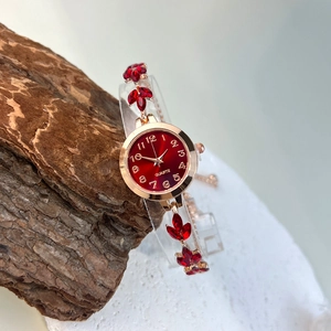 Macro shot of rose gold quartz watch with red leaf crystal bracelet on wooden background