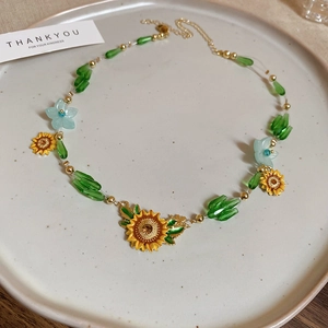 Detailed view of sunflower and bee necklace with yellow enamel pendants and green beads