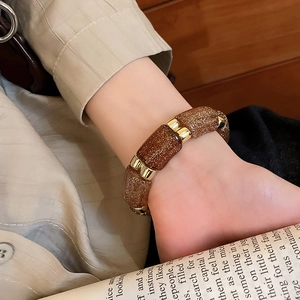 Detail of amber resin geometric bracelet with gold metallic beads on a model's wrist