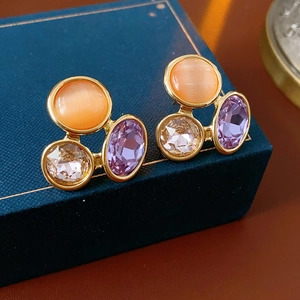 Detail of vintage oval earrings with orange cat-eye stone and purple crystals in gold frame