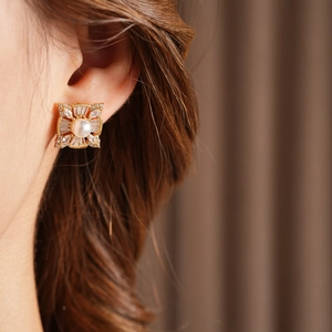 Detail of a model wearing a gold square earring with a large pearl and sparkling zircons