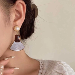 Close-up of geometric resin and pearl drop earrings worn on a model for retro style