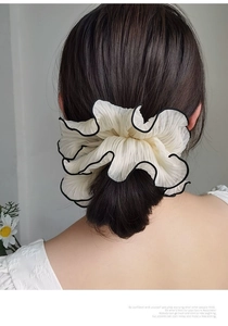 Detail of cream white pleated scrunchie with black trim shown on tied hair