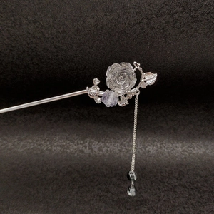 Detailed silver rose hair pin with metallic tassel and shimmering petals on dark background