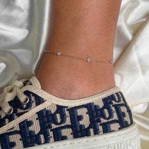 Detail of rose gold flower anklet with purple clover charms on model ankle