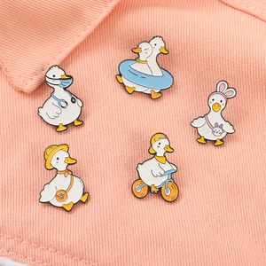 Five cartoon duck enamel pins with doctor, swimming and cycling themes on pink fabric