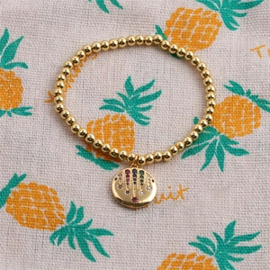 Detail of gold beaded elastic bracelet with a radiant multi-colored zircon palm pendant