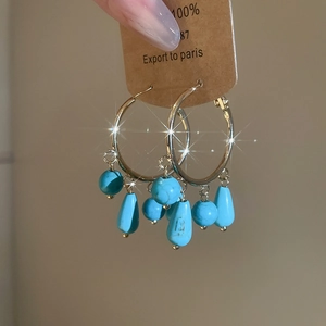Detail of gold hoop earrings with blue stone drop charms on a kraft paper card