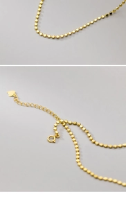 Detail of gold flat bead chain with heart charm and spring clasp on silver necklace