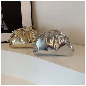 Detail of metallic pleated cloud clutch bags in gold and silver on a beige display stand