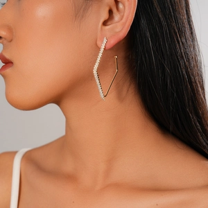 Detailed close-up of a gold geometric diamond earring worn by a model in soft lighting