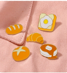 Gros plan de cinq broches en émail en forme de pain sur un fond en tissu rose texturé