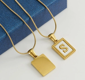 Detail view of 18K gold snake chain necklaces with rectangle pendants and letter S
