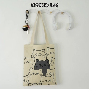 Detailed close-up of a beige knitted shoulder bag with a black cartoon cat pattern